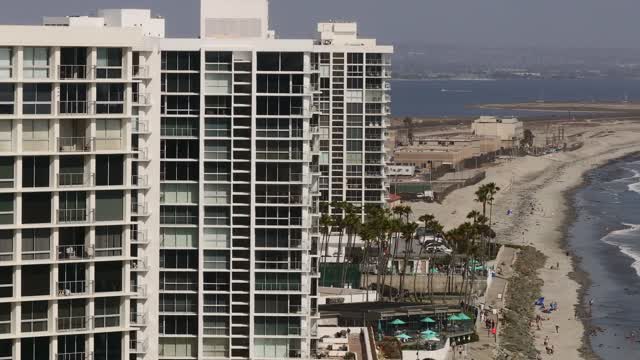 Low aerial view of the beach, palm trees and the ocean at Coronado Beach, with people walking.