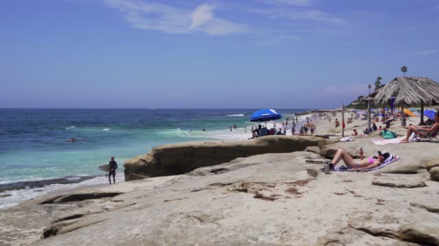 Elevated view of the beach, the surf and palm trees at Windansea, with a crowd gathered.