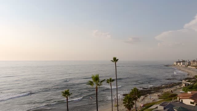 Low aerial view of the beach, the surf and palm trees at Beach Barber Tract, with people walking.