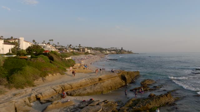 Low aerial view of the beach, the ocean and homes at Beach Barber Tract, with a crowd gathered.