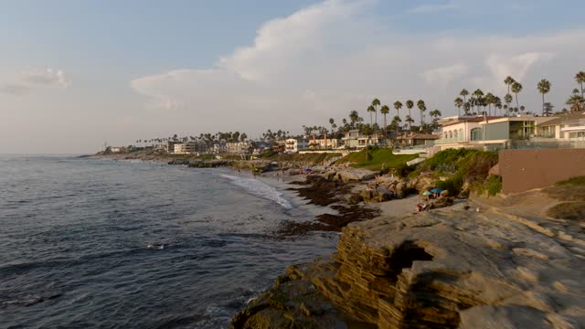 Low aerial view of the cliffs, palm trees and the ocean at Beach Barber Tract, with people walking.