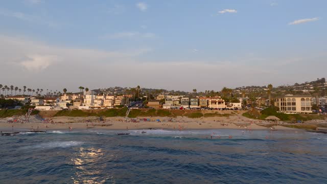 Low aerial view of the beach, the surf and palm trees at Beach Barber Tract, with people walking.