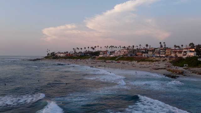 Low aerial view of the beach, the surf and palm trees at Beach Barber Tract, with people walking.