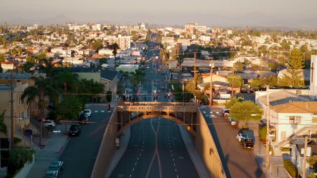 Low aerial view of a residential street, the bridge and palm trees in North Park, with people walking.