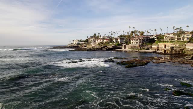 Low aerial view of the cliffs, the surf and palm trees at Bird Rock.