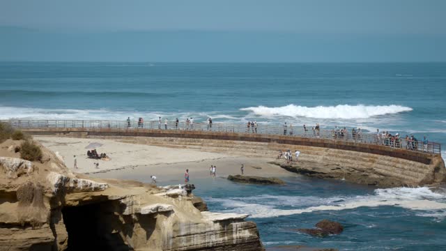 Elevated view of the beach, the surf and the ocean at La Jolla Cove, with people walking.