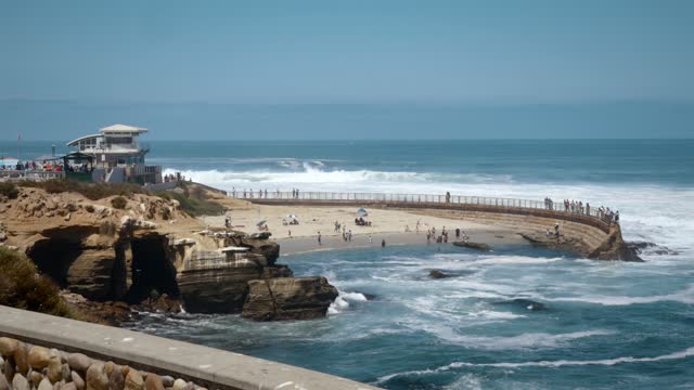 Elevated view of the cliffs, the surf and the ocean at La Jolla Cove, with a crowd gathered.