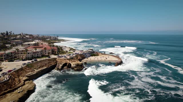 Aerial view of the cliffs, the surf and palm trees at La Jolla Cove, with people walking.