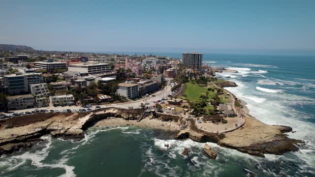 Aerial view of the cliffs, the surf and the ocean at La Jolla Cove, with people walking.