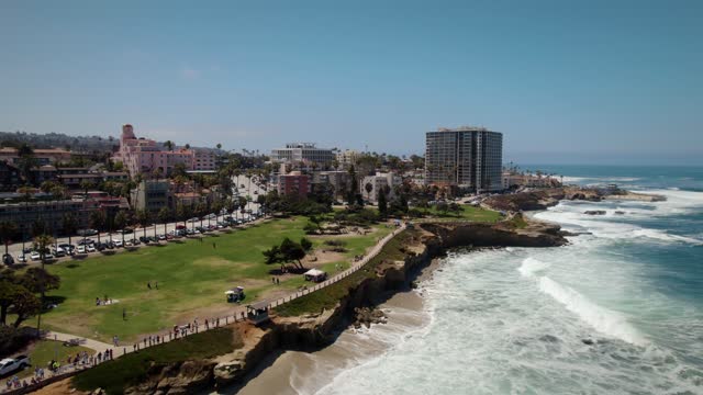 Aerial view of the cliffs, the surf and palm trees at La Jolla Cove, with people walking.