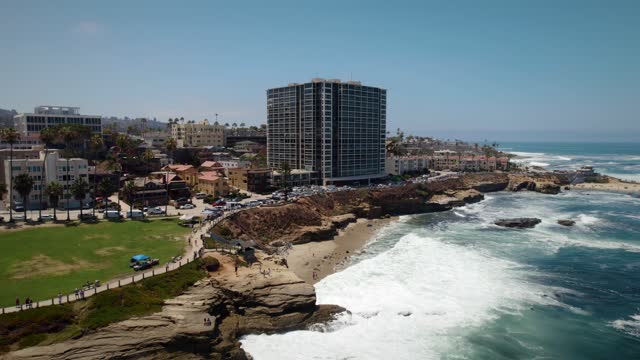 Aerial view of the cliffs, the surf and palm trees at La Jolla Cove, with people walking.