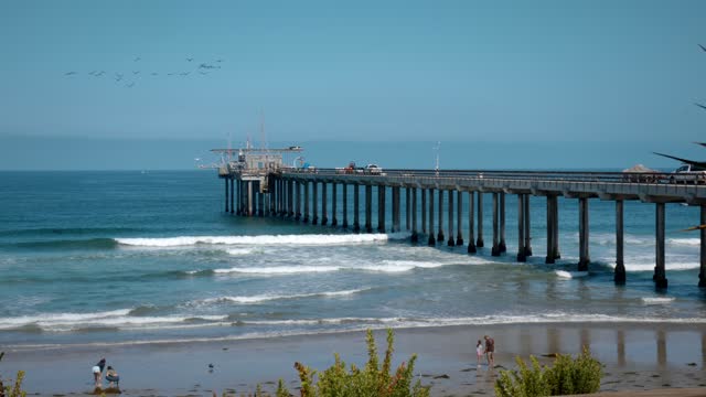The beach, the surf and the pier at La Jolla Shores, with people walking.