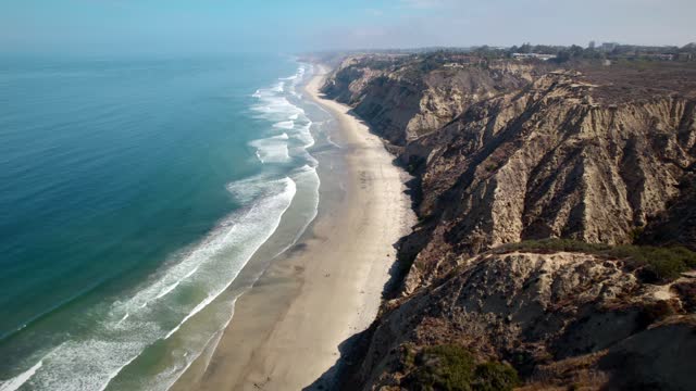 Aerial view of the cliffs, the surf and the ocean at Black’s Beach, with people walking.