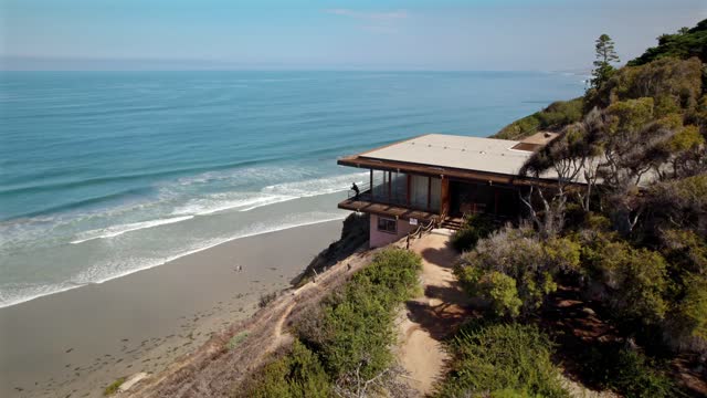 Low aerial view of the cliffs, the surf and the ocean at Black’s Beach, with people walking.