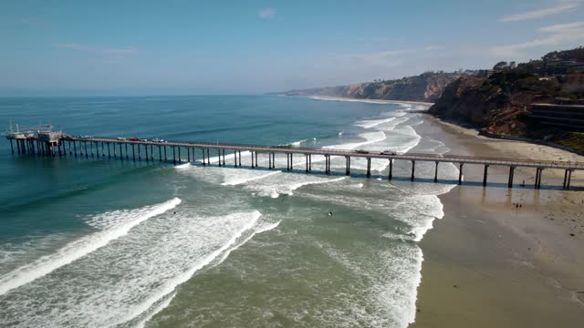 Aerial view of the beach, the surf and the pier at La Jolla Shores, with surfers out.