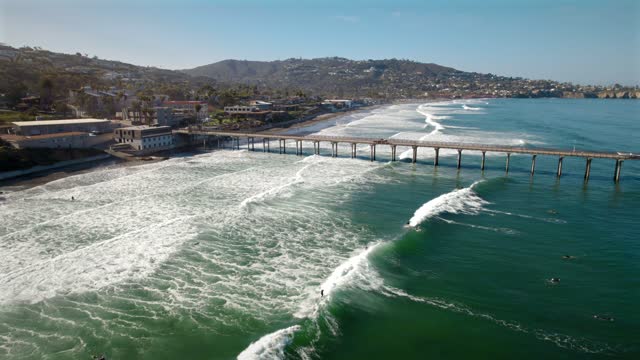 Aerial view of the beach, the surf and the pier at La Jolla Shores, with surfers out.