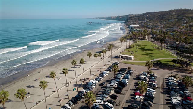 Low aerial view of the beach, the surf and the pier at La Jolla Shores, with people walking.