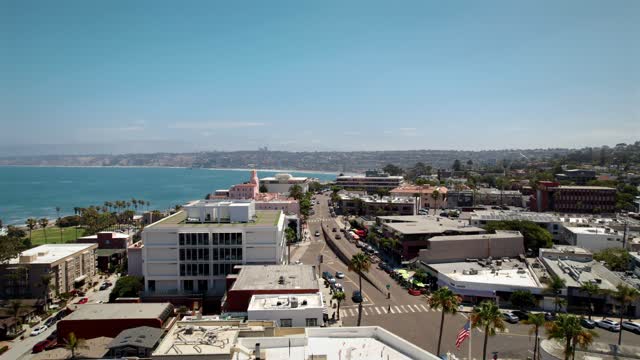Low aerial view of the downtown streets, palm trees and the ocean at La Jolla Village, with people walking.