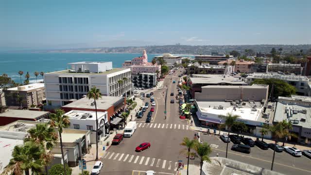 Low aerial view of the downtown streets, palm trees and the ocean at La Jolla Village, with people walking.