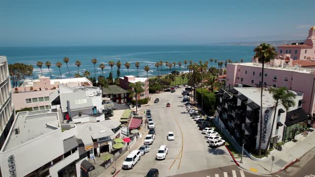 Low aerial view of the downtown streets, palm trees and the ocean at La Jolla Village, with people walking.