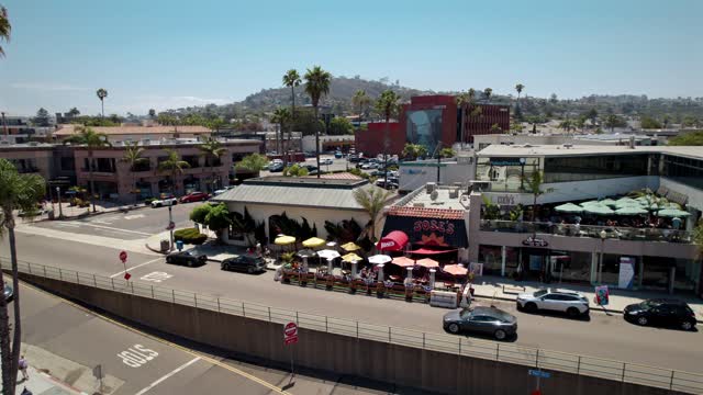 Low aerial view of the downtown streets, palm trees and the buildings at La Jolla Village, with people eating outside.