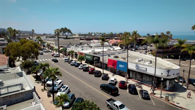Low aerial view of the downtown streets, palm trees and the ocean at La Jolla Village, with people walking.