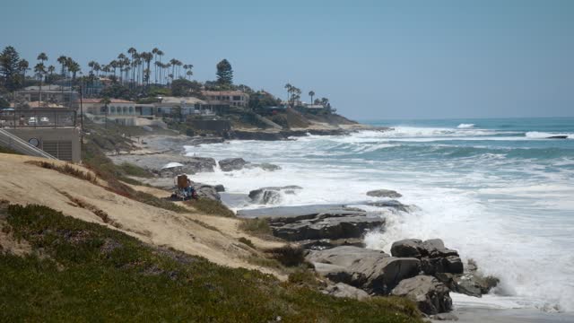 Elevated view of the cliffs, the surf and palm trees at Windansea, with people walking.