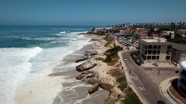 Low aerial view of the beach, the surf and palm trees at Windansea, with people walking.