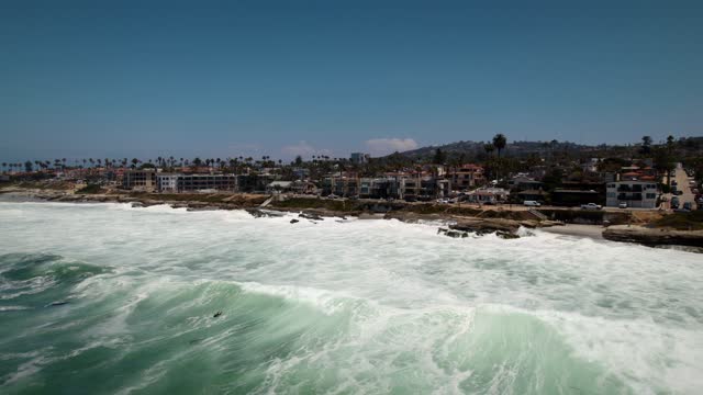Low aerial view of the beach, the surf and palm trees at Windansea, with surfers out.
