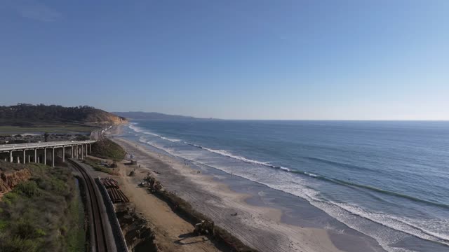 Aerial view of the cliffs, the surf and the bridge in Del Mar, with people walking.