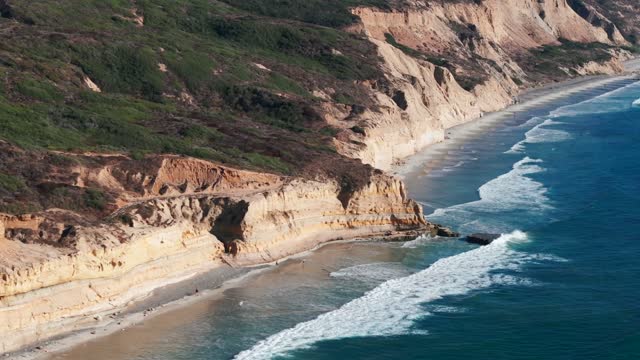 Aerial view of the cliffs, the surf and the ocean at Torrey Pines, with people walking.