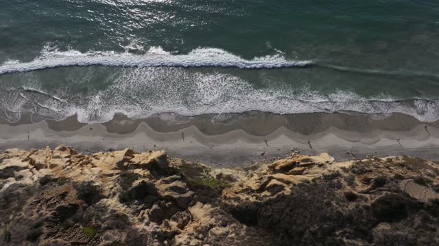 Aerial view of the cliffs, the surf and the ocean at Torrey Pines, with people walking.