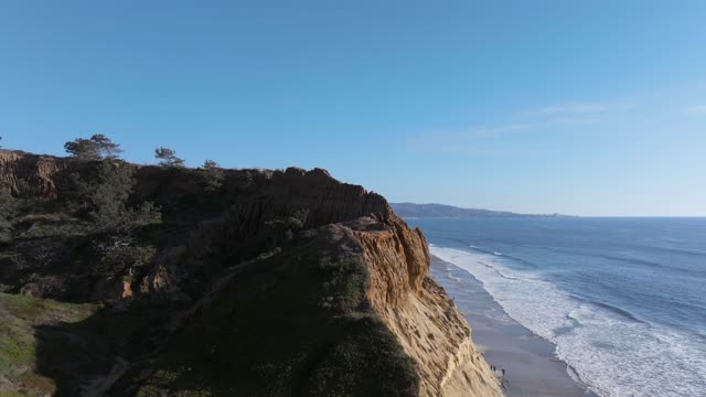 Low aerial view of the cliffs, the surf and the ocean at Torrey Pines, with people walking.