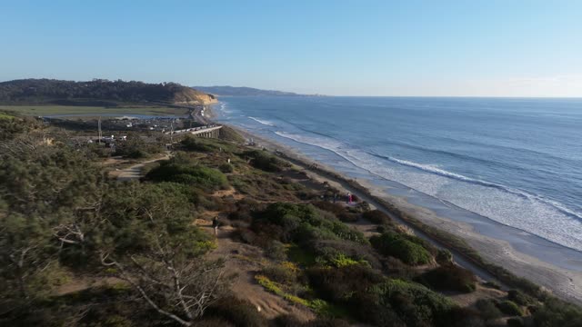 Aerial view of the cliffs, the surf and the ocean in Del Mar, with people walking.