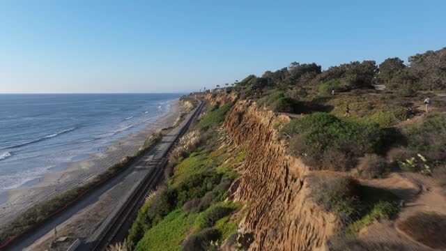 Low aerial view of the cliffs, the surf and the ocean in Del Mar, with people walking.