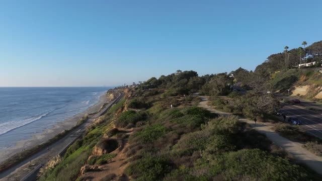 Low aerial view of the cliffs, palm trees and the ocean in Del Mar, with people walking.