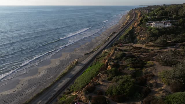 Aerial view of the cliffs, the surf and the ocean in Del Mar, with people walking.