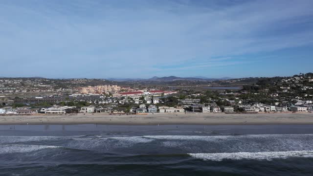 Low aerial view of the beach, the surf and palm trees in Del Mar, with people walking.