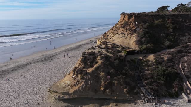 Aerial view of the cliffs, the surf and the ocean at Del Mar Dog Beach, with people walking.