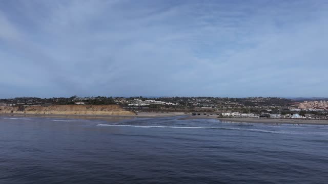 Low aerial view of the cliffs, the ocean and homes at Del Mar Dog Beach.