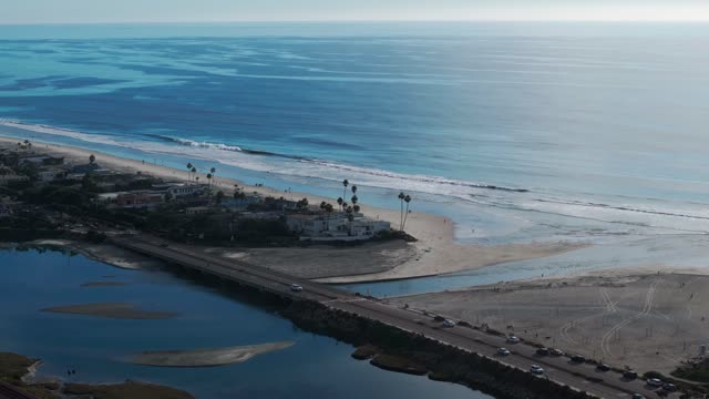 Aerial view of the beach, the surf and the bridge in Del Mar, with people walking.