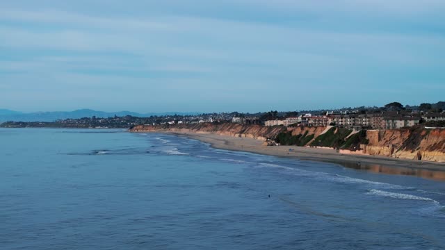 Low aerial view of the beach, the ocean and homes at Del Mar Dog Beach, with people walking.
