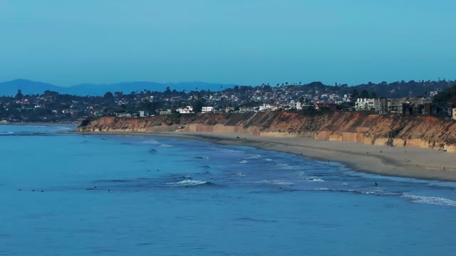 Aerial view of the beach, the surf and the ocean at Del Mar Dog Beach, with surfers out.