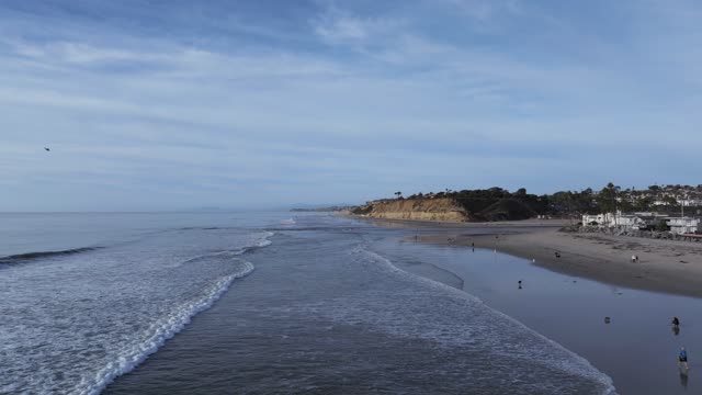Low aerial view of the beach, the surf and the ocean at Del Mar Dog Beach, with people walking.