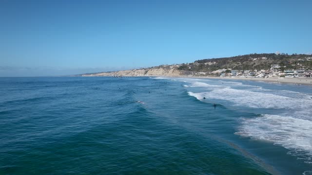 Low aerial view of the beach, the surf and the ocean at La Jolla Shores, with surfers out.