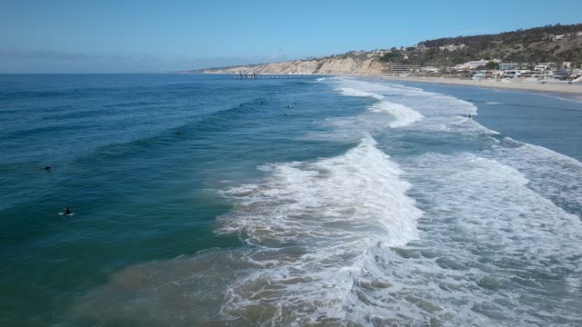 Low aerial view of the beach, the surf and the ocean at La Jolla Shores, with surfers out.