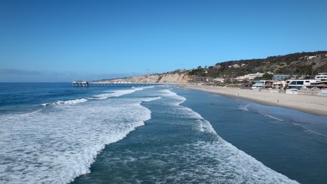Low aerial view of the beach, the surf and the pier at La Jolla Shores, with people walking.
