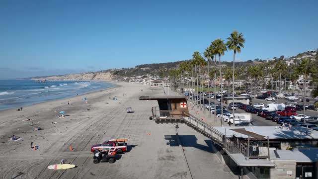 Low aerial view of the beach, the surf and palm trees at La Jolla Shores, with people walking.
