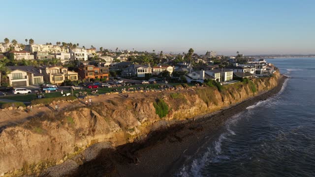 Low aerial view of the cliffs, palm trees and the ocean at Bird Rock, with people walking.