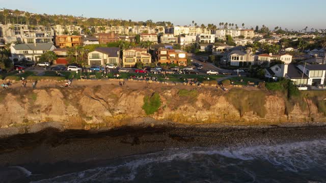 Low aerial view of the cliffs, palm trees and the ocean at Bird Rock, with a crowd gathered.